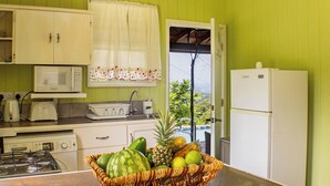 A kitchen with a microwave, toaster, sink, and refrigerator. A basket of fruit is on the counter.