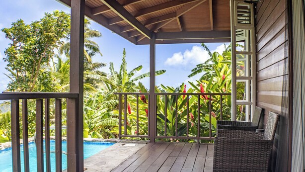 A wooden deck with a pool, surrounded by tropical plants and a covered seating area.