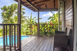 Una terrazza in legno con piscina, circondata da piante tropicali e una zona relax coperta.