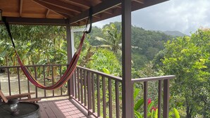 A wooden deck with a hammock, wicker furniture, and a view of lush greenery and a pool.