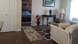 A living room with a sofa, a table, a vase with flowers, a painting on the wall, and a door leading to a bedroom. - Beautiful 4 BR/2BA Private Pool Home Near Weeki Wachee Springs (Spring Hill, Florida, 34608)