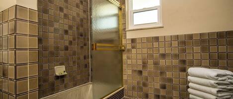 Une salle de bain avec une douche à parois de verre, des murs carrelés, une petite fenêtre et une pile de serviettes.