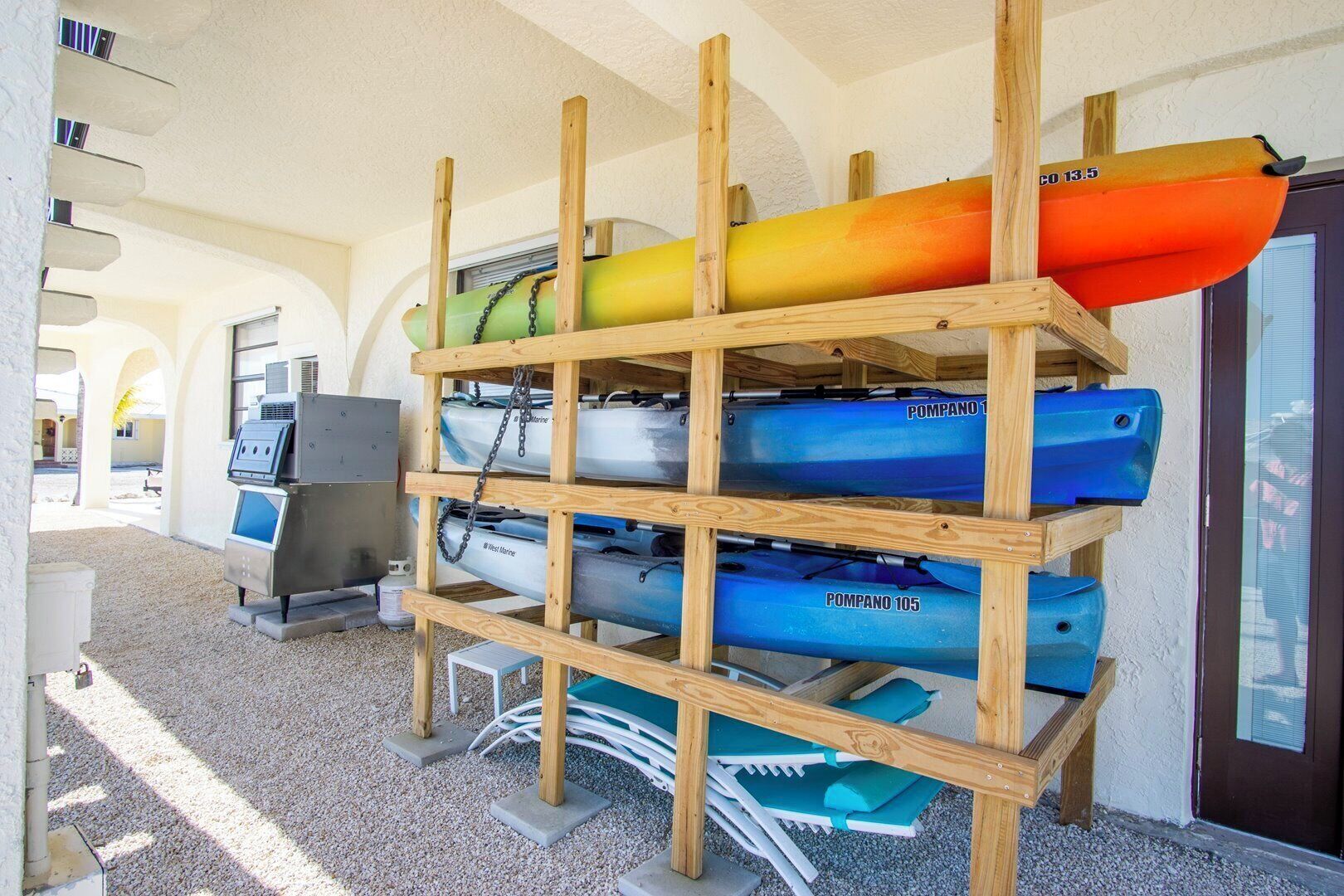 Un portarocce in legno con kayak e tavole da paddleboard, un barbecue e una porta con oblò.