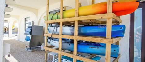 Un portarocce in legno con kayak e tavole da paddleboard, un barbecue e una porta con oblò.