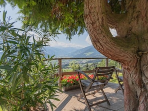 Eine hölzerne Bank mit Metallgestell, auf einer gefliesten Terrasse mit Blick auf Berge und Grünflächen.