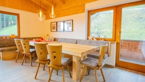 Un comedor moderno con una mesa y sillas de madera, ventanas amplias con vistas a zonas verdes, y techo de madera.