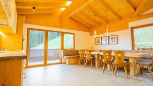 Una cocina amplia con vigas de madera, un comedor con sillas y ventanas grandes que ofrecen vistas al exterior.