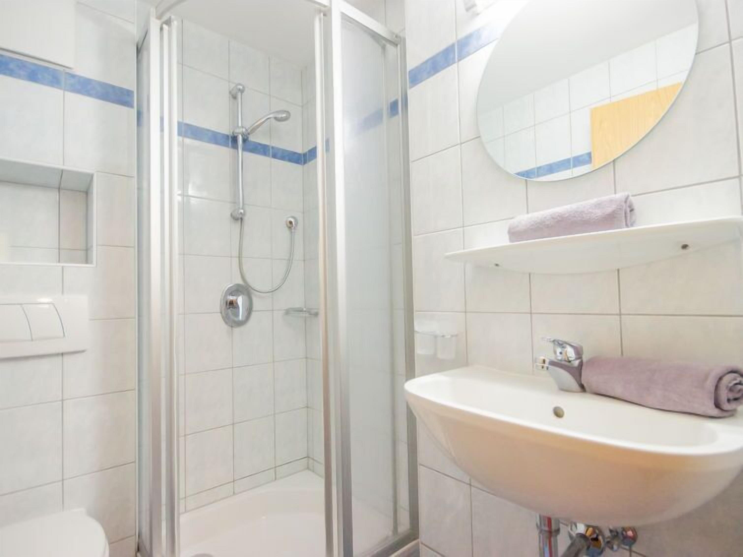 Une salle de bain avec une douche à parois de verre, un lavabo avec un miroir au-dessus et une serviette accrochée au mur.
