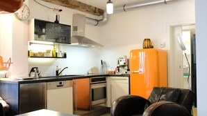 A compact kitchen with a dishwasher, oven, and a bright orange refrigerator.