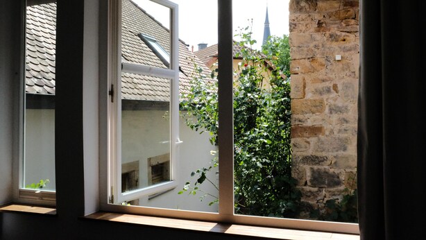 A window with a view of a stone wall and a building with a tiled roof.