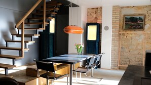 A modern kitchen with a wooden staircase, a dining table with chairs, and a hanging pendant light.