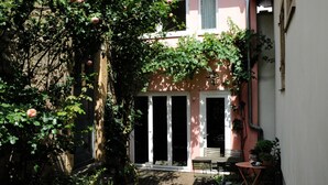 A courtyard with a pink building, a wooden bench, and a small table.