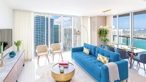 Una sala de estar moderna con un sofá azul, una mesa de centro y un comedor con vistas a la ciudad.