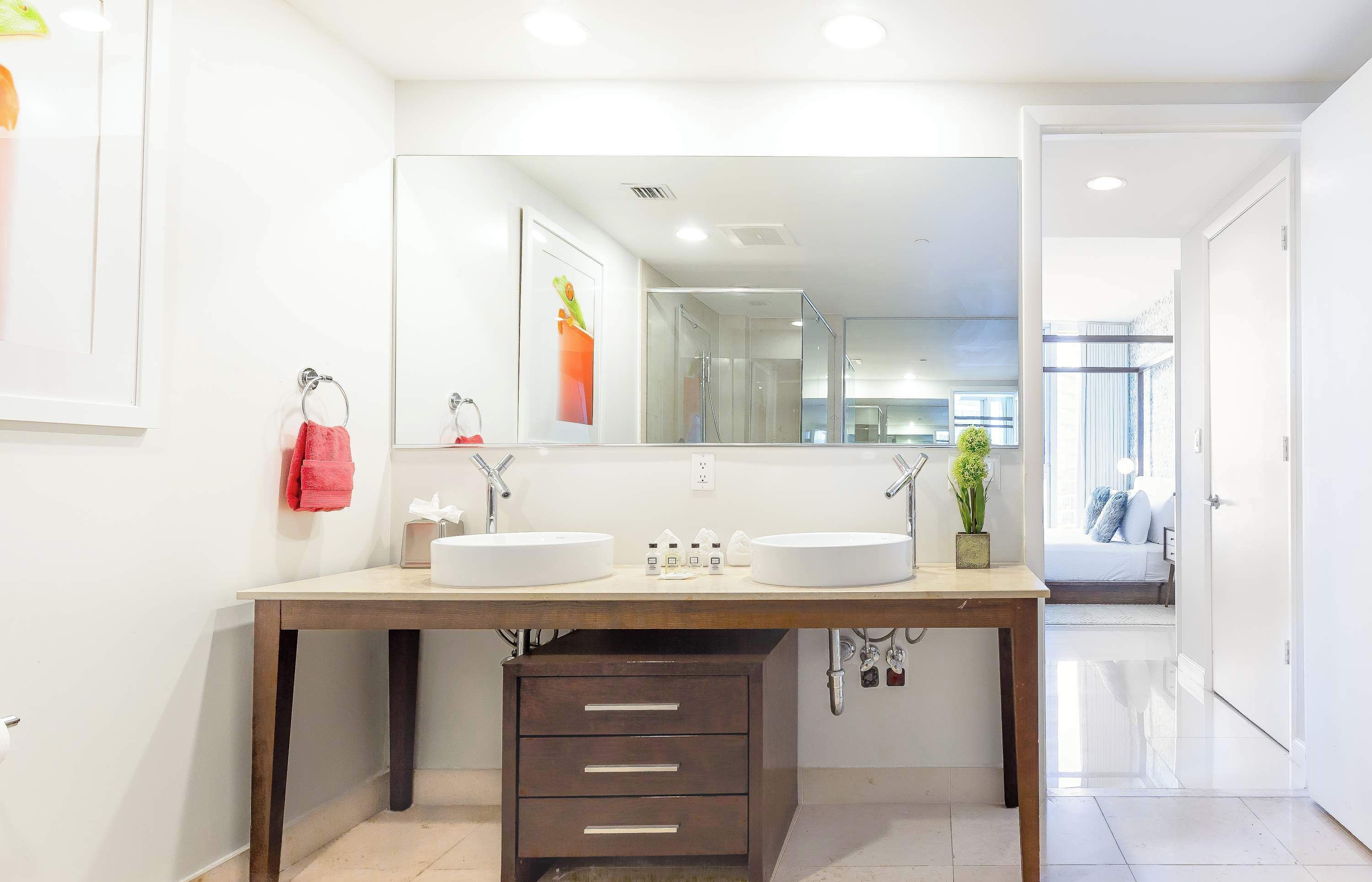 A modern bathroom with two sinks, a large mirror, and a wooden vanity.