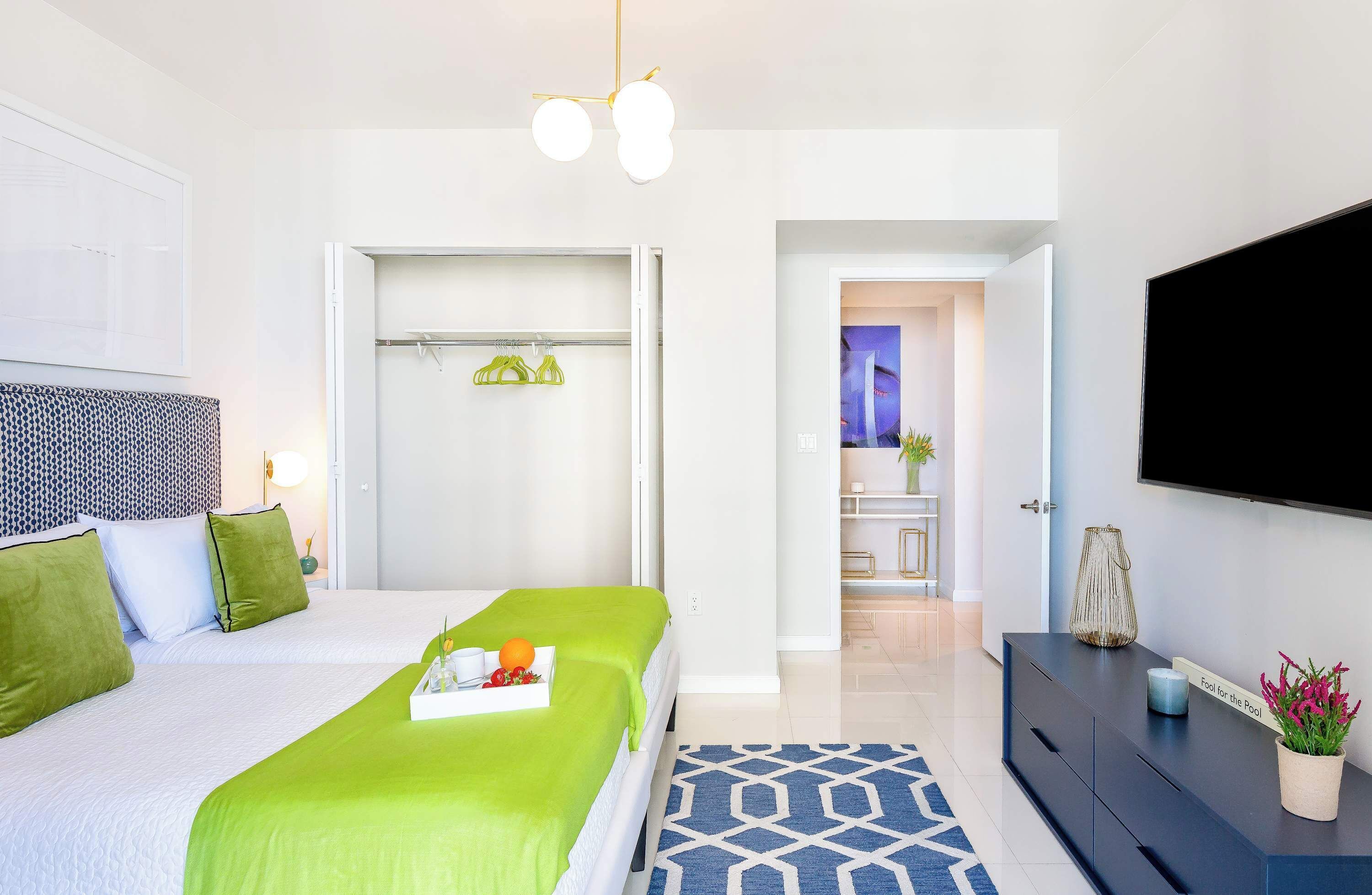 A modern hotel room with a bed, a TV, a wardrobe, and a bathroom visible through an open door.