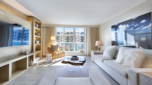 Habitación de hotel moderna con un ventanal grande, un televisor de pantalla plana, un sofá, una mesita de café y una estantería.