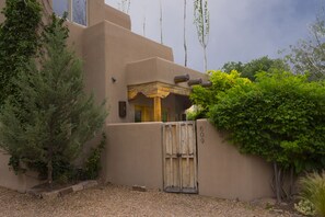 Stucco exterior and lush garden surround this charming residence, featuring a covered entryway and multiple windows.