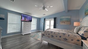 Un dormitorio con cama, cómoda, televisor y ventilador de techo.