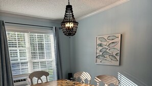 Ein Esszimmer mit einem Holztisch, weißen Stühlen, einer Pendelleuchte und einem Kunstwerk mit Fischmotiv an der Wand.