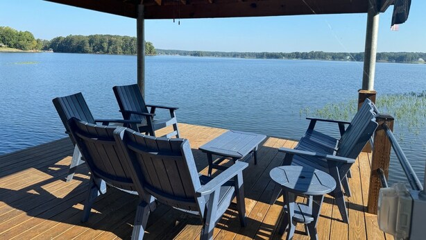Eine Holzterrasse mit Stühlen und Tischen, die auf einen ruhigen See blickt, mit einem überdachten Bereich.