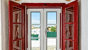 A room with a white wall, a wooden floor, and a window with red shutters. - Veiros House / Estremoz II (Veiros)