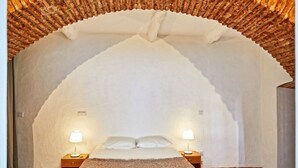A bedroom with a vaulted ceiling, a bed with two pillows, two bedside tables with lamps, and a fluffy rug. - Veiros House / Estremoz II (Veiros)