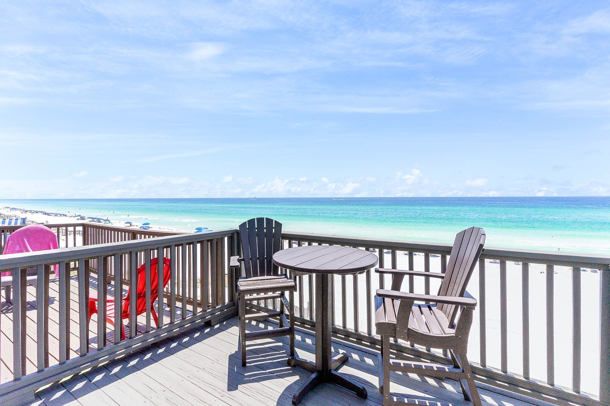 Une terrasse avec une table et deux chaises Adirondack donnant sur une plage.