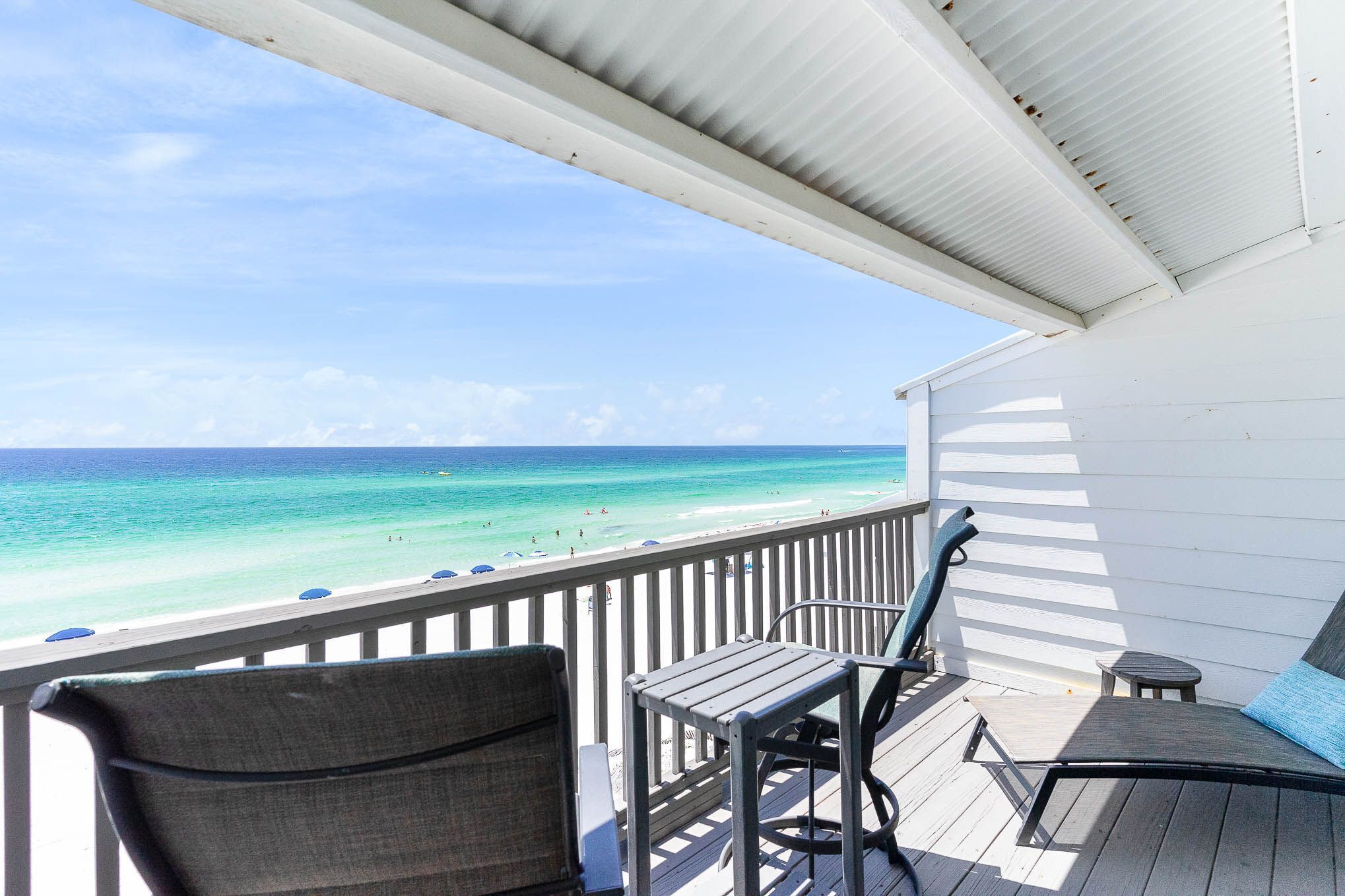 A deck with a view of the ocean, a white railing, and a small table and chair.