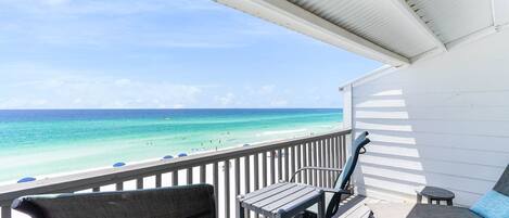 A deck with a view of the ocean, a white railing, and a small table and chair.