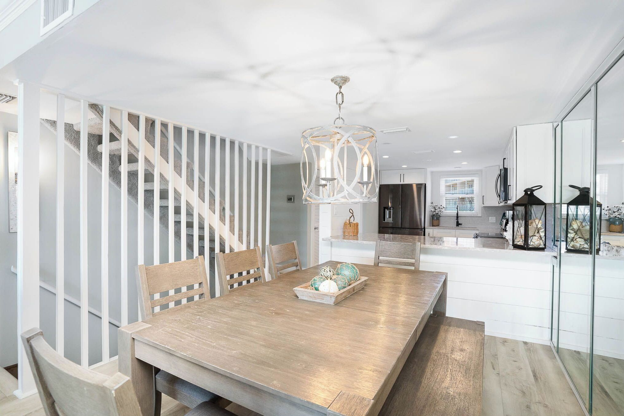 A modern kitchen with white cabinetry, a wooden dining table with chairs, and a hanging light fixture.