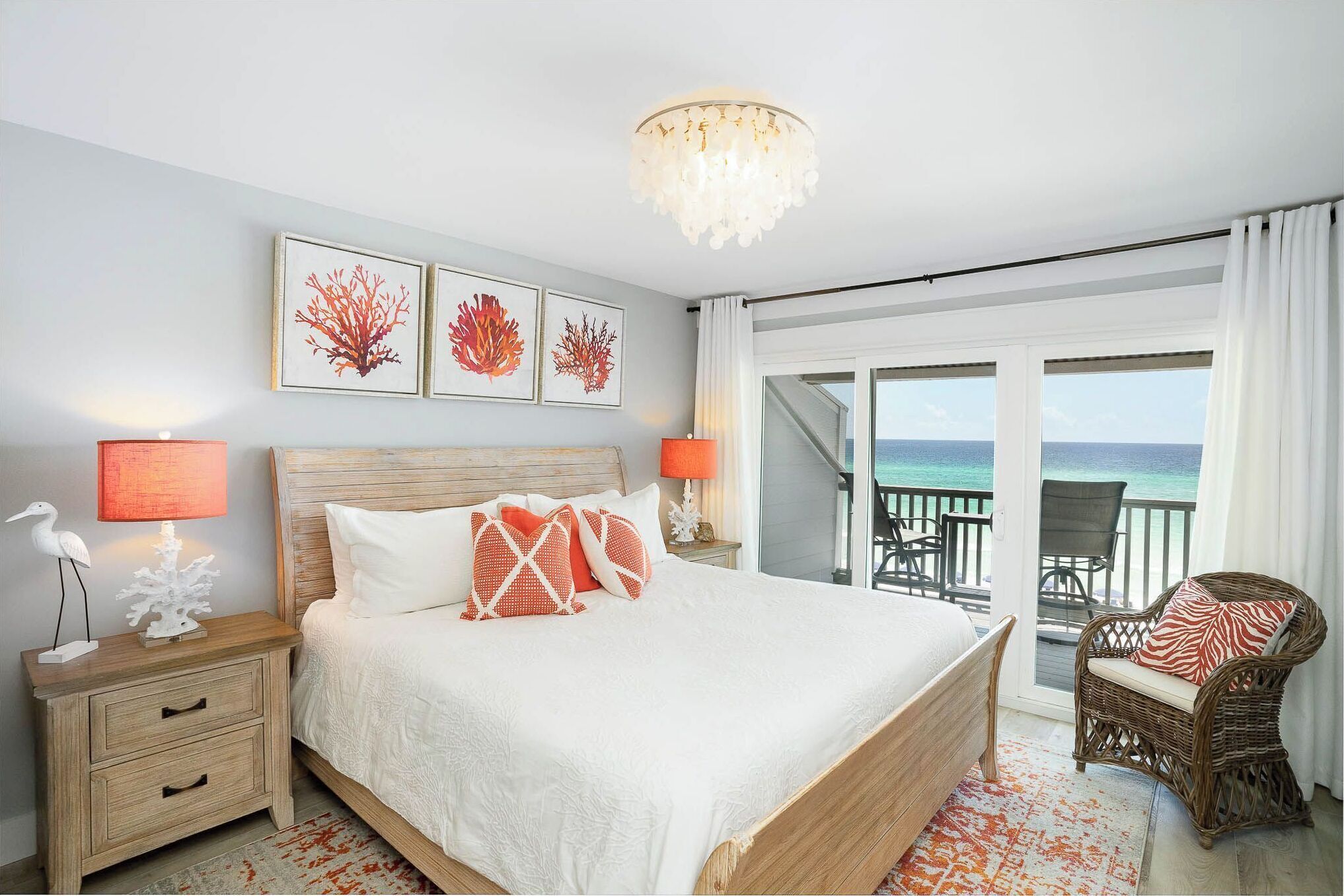 A bedroom with a large bed, two bedside lamps, a nightstand, and a view of the ocean through a sliding door.