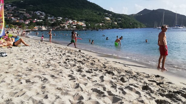 Una playa con gente nadando y caminando por la orilla.