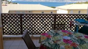 Un balcón con vista al mar y a las montañas, una mesa con mantel floral y un ventilador de techo.
