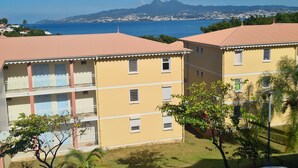 Un edificio amarillo con balcones y vistas al mar y a las montañas al fondo.
