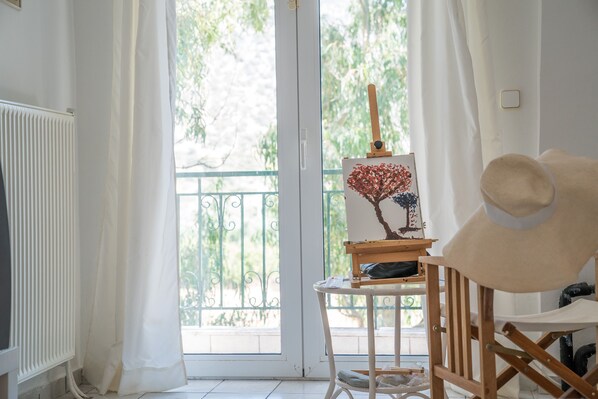 A room with a radiator, a window with curtains, a wooden chair, and a small table with a painting.