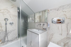 A modern bathroom with a glass-enclosed shower, a white sink, and a marble backsplash.