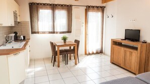 A small, well-lit kitchen with a dining area, a television on a wooden stand, and a window with curtains. - Aurore du Lac - Duplex Apartment 4pers. + Studio 2pers. (Sevrier)