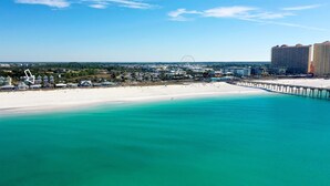 Une vue sur la côte, avec une plage de sable, une eau turquoise et limpide, et une jetée qui s’avance dans la mer.