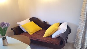 Una habitación acogedora con un sofá cama de madera, una mesita y un florero con flores.