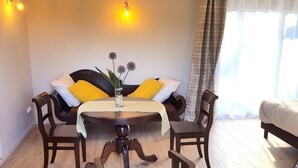 Una habitación acogedora con una mesa redonda, dos sillas, un sofá con cojines amarillos y un jarrón con flores.