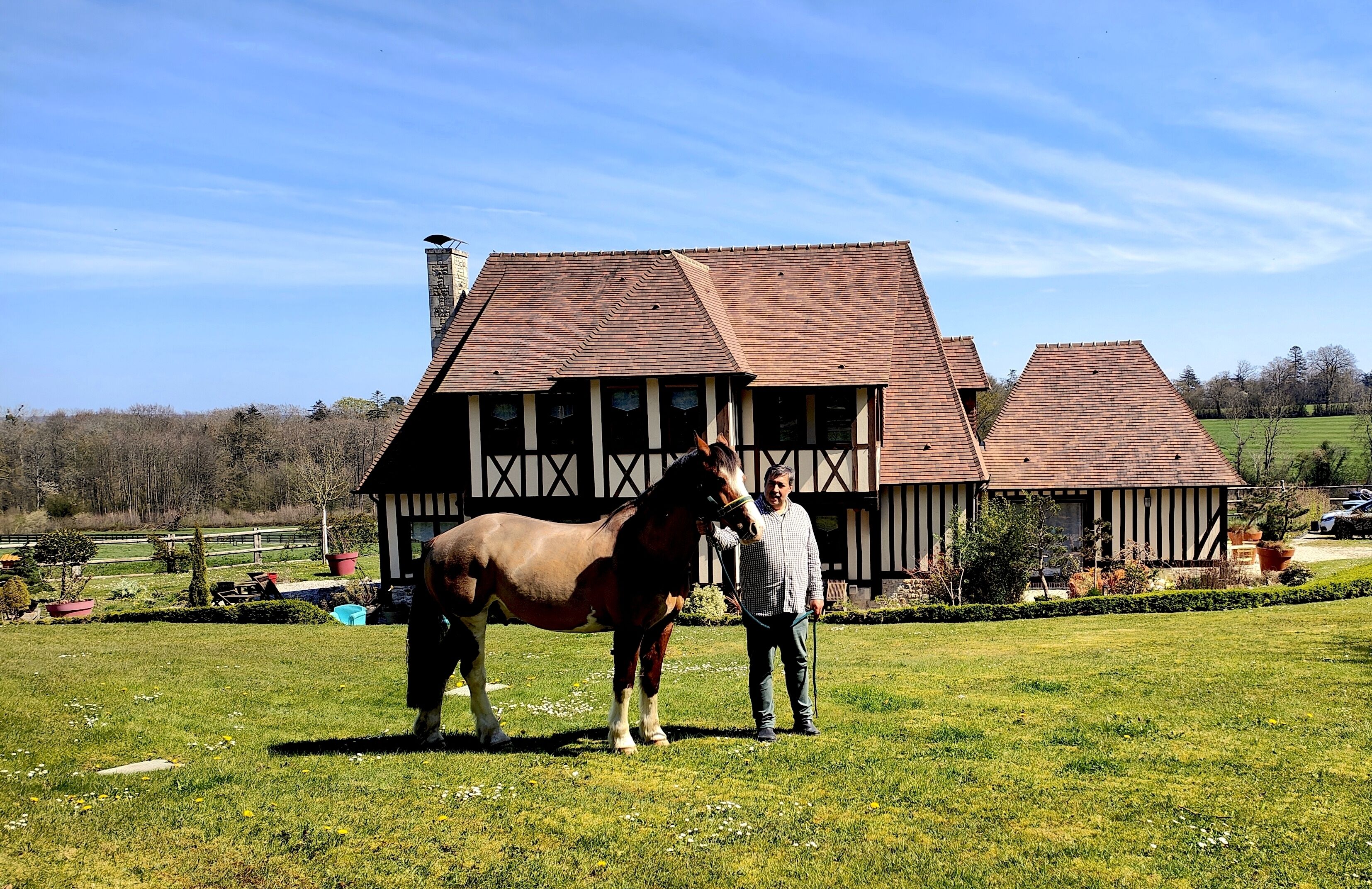 Een stal met een paard en een persoon voor een groot, traditioneel gebouw met een schuin dak.