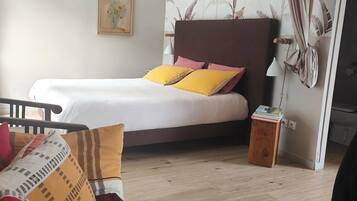 Une chambre à coucher avec un lit, des oreillers, une table de chevet, un plancher en bois, un tableau au mur et un rideau.