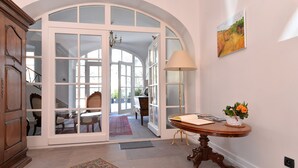 Un vestíbulo amplio con un gran portón de cristal arqueado que da a un comedor, una mesa de madera con una lámpara y un cuadro en la pared.