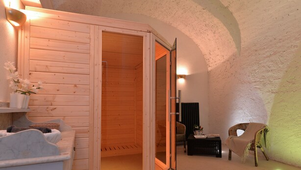 Un sauna de madera con puerta corrediza, una silla de mimbre y una mesita con lámpara.