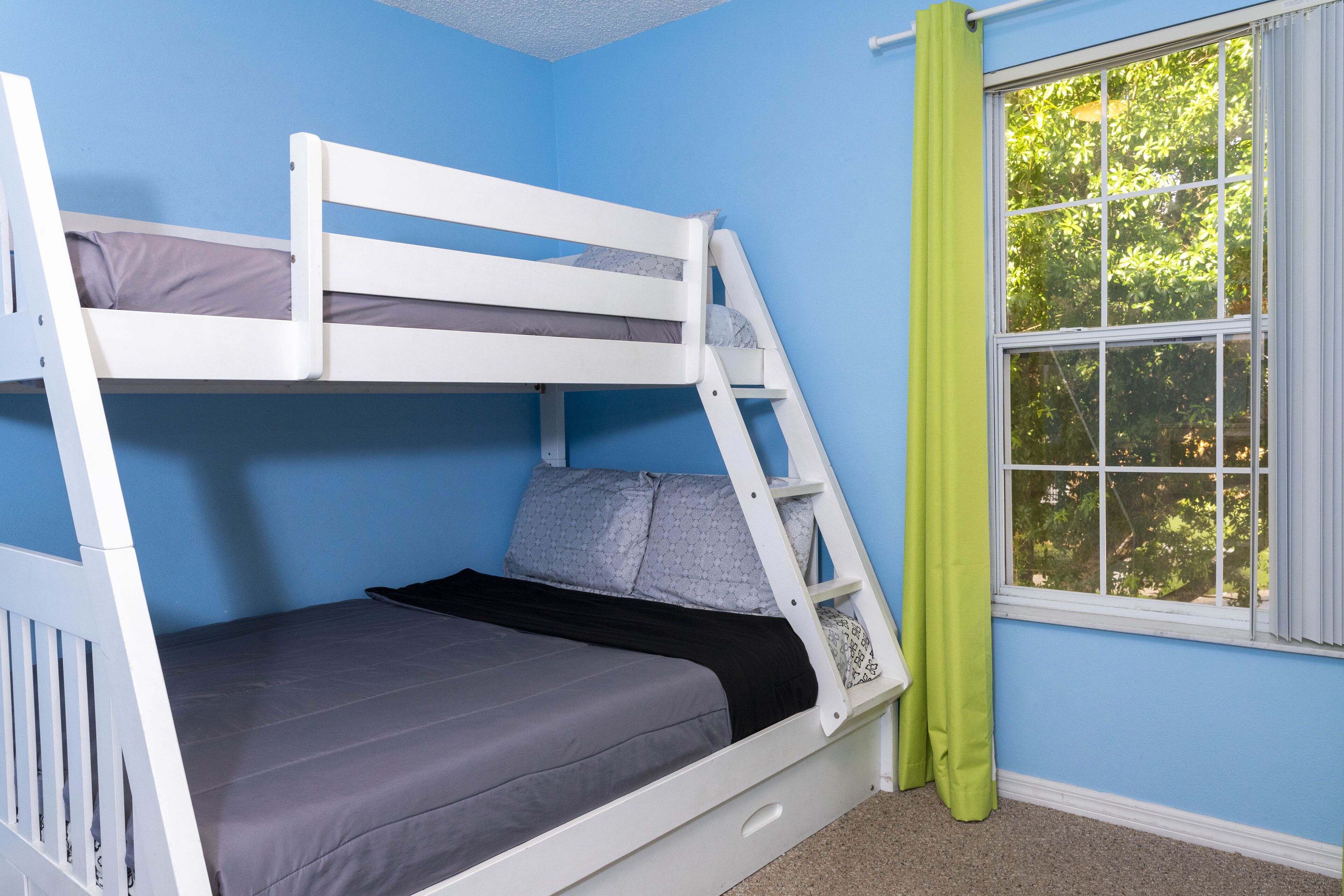 Ein Stockbett in einem Zimmer mit blauen Wänden und einem Fenster mit grünen Vorhängen.