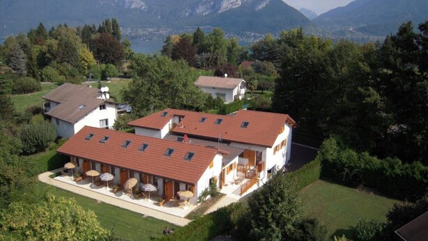 Un bâtiment à deux étages, doté d’un toit recouvert de tuiles rouges, d’un espace extérieur abrité avec des parasols, et offrant une vue sur les montagnes en arrière-plan.