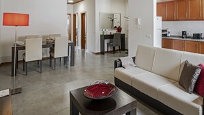 A modern living room with a sofa, dining table, and chairs. There is a kitchen area with wooden cabinets and a countertop.