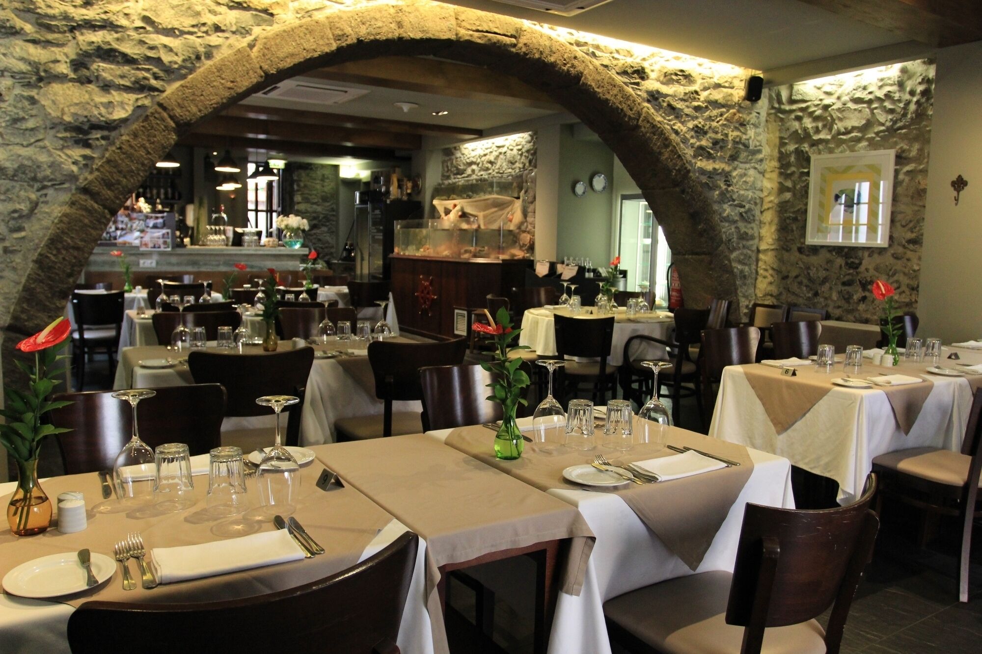 A restaurant with stone arches, tables set with white tablecloths, and a bar area in the background.