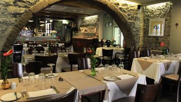 A restaurant with stone arches, tables set with white tablecloths, and a bar area in the background.