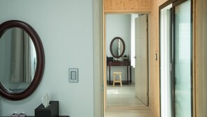 Un pasillo con paredes de madera, un espejo, un taburete pequeño y una puerta que da a otra habitación.